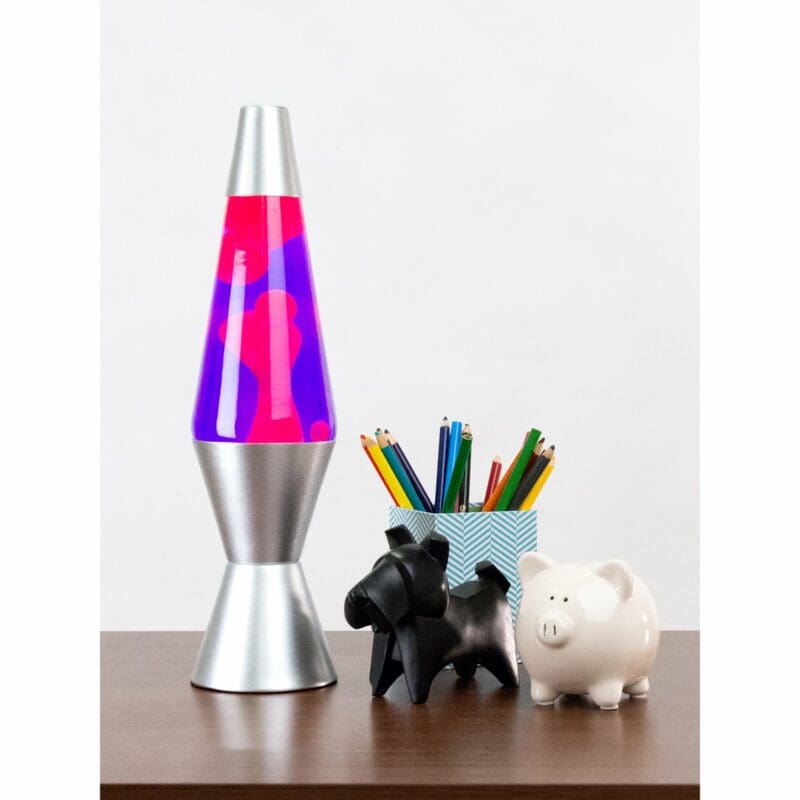 21210401US-LavaLamp-14-5-Pink-and-Purple-web 14.5” LAVA® Lamp – Pink/Purple/Silver on table with pencil cup, scotty dog figure, and white piggy bank